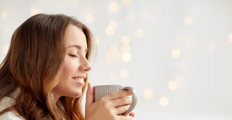 Mulher sorri de olhos fechados segurando uma xícara
